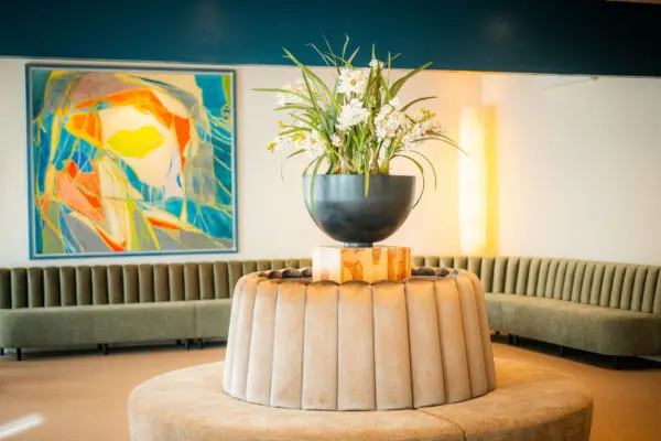 Gebogen zitbank met een ronde tafel, hangplant en kleurrijk schilderij in de familiekamer.