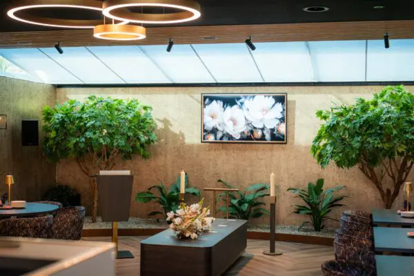 Koffiekamer met ronde plafondlampen, tafels en een groene wand met beeldscherm.