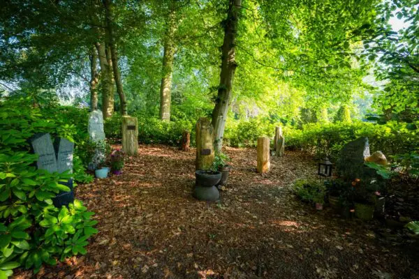 Gedenkbeeld tussen bomen en groene beplanting in de bostuin van Crematorium Kranenburg.