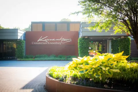 Voorkant en logo van Crematorium Kranenburg met bloemen en groene beplanting.