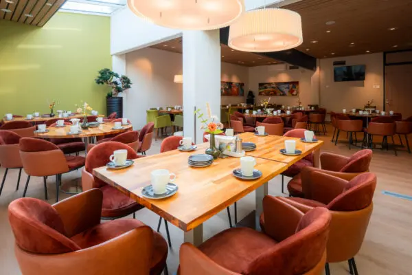 Gedekte houten tafel met kopjes en gestoffeerde stoelen in de koffiekamer.
