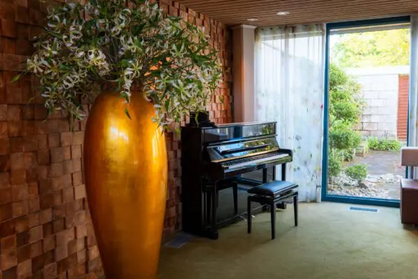 Piano naast een grote gouden vaas en een raam met uitzicht op het groen.