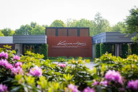 Naambord van Crematorium Kranenburg tussen bloeiende planten.