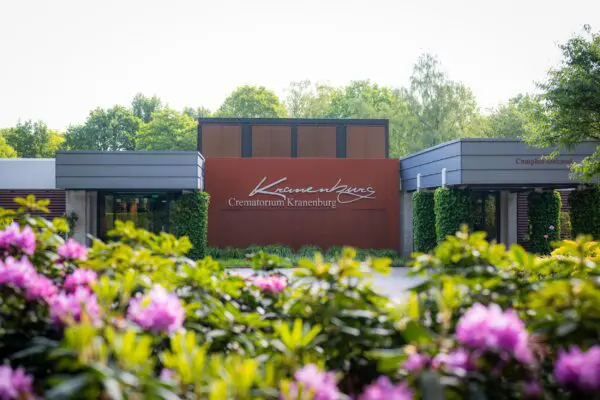 Naambord van Crematorium Kranenburg tussen bloeiende planten.