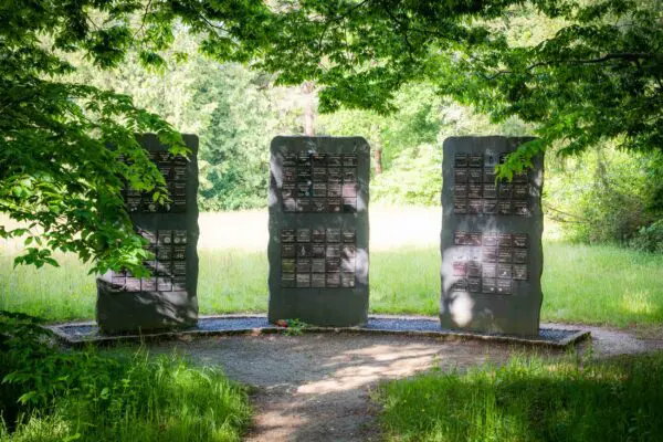 Rechtopstaande gedenkpanelen tussen bomen en groene beplanting.