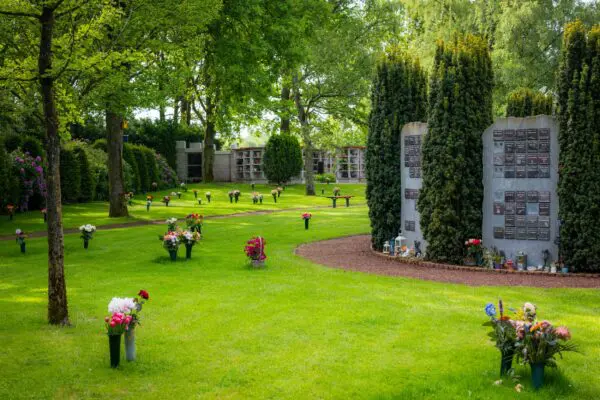 Groene gedenktuin met bloemstukken en rechtopstaande gedenkpanelen.