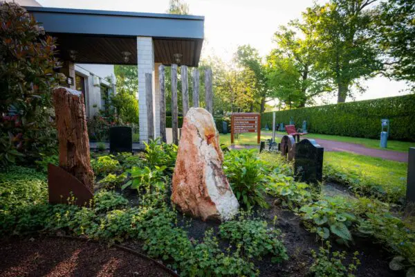 Houten gedenkobject en stenen gedenkobject in het groen naast Crematorium Kranenburg.