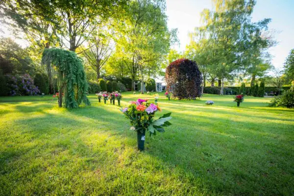 Groene gedenktuin met bloemstukken en een klein herdenkingsgebouw.