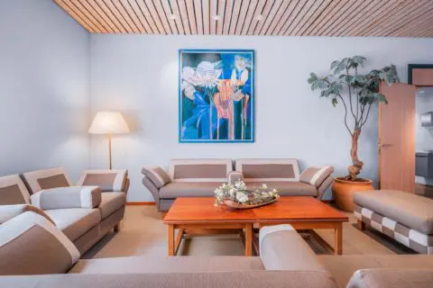 Familiekamer met lichte banken rond een houten tafel en een kleurrijk schilderij.