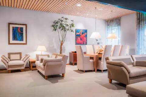 Familiekamer met lichte fauteuils, tafellampen en kleurrijke kunst aan de wand.