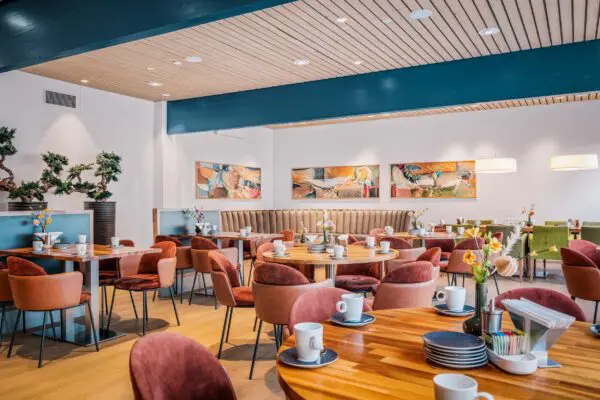 Koffiekamer met houten tafels, kopjes en verschillende zitplaatsen.