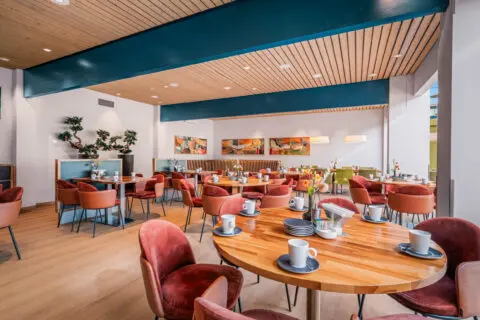 Houten tafels met kopjes en roodbruine stoelen in de koffiekamer.