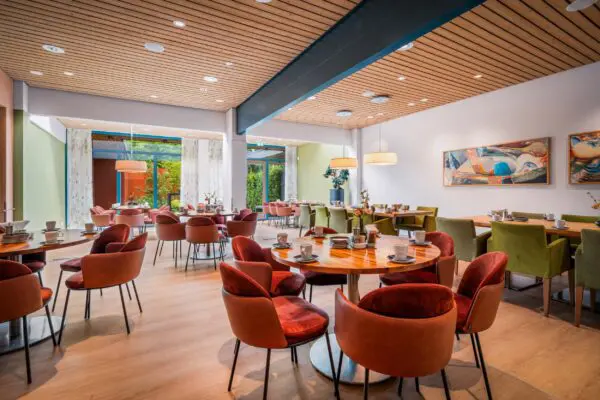 Koffiekamer met ronde tafels, roodbruine stoelen en kunstwerken aan de wand.