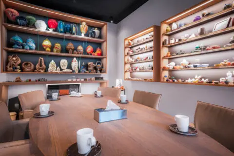 Toonkamer van Crematorium Kranenburg met een houten tafel en wandkasten met urnen en gedenkobjecten.
