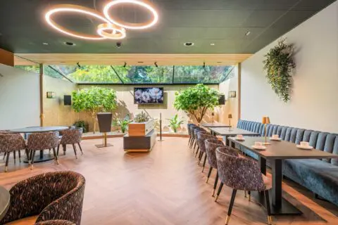 Ronde tafels en stoelen in de tuinkamer onder cirkelvormige plafondlampen.