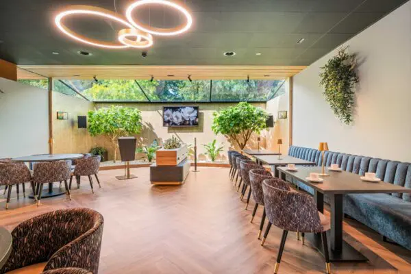 Ronde tafels en stoelen in de tuinkamer onder cirkelvormige plafondlampen.