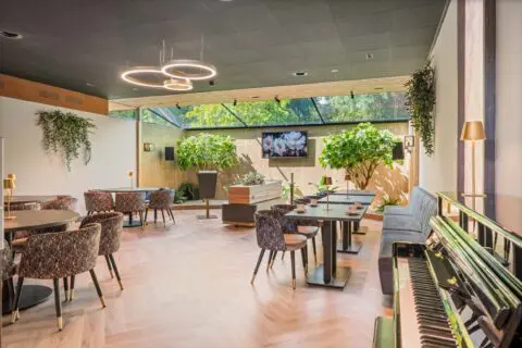 Tuinkamer met ronde tafels, houten stoelen en een groene afbeelding aan de wand.