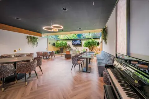 Tuinkamer met houten tafels, verschillende zitplaatsen en uitzicht op de tuin.